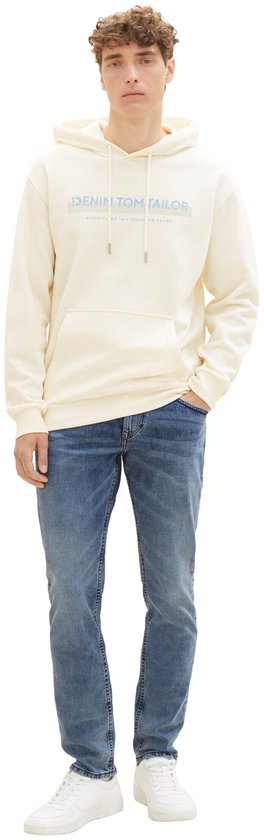 Man in crème hoodie met 'DENIM TOM TAILOR' opdruk en slanke, lichtblauwe spijkerbroek.