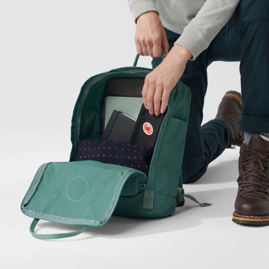 Open groene Fjällräven Kånken rugzak met inhoud: tijdschrift, notitieboekjes en een trui.