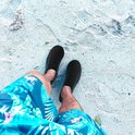 Bovenaanzicht van voeten op het strand, dragend zwarte waterschoenen met blauwe spetters.