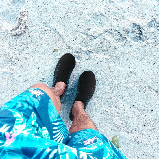 Bovenaanzicht van voeten op het strand, dragend zwarte waterschoenen met blauwe spetters.