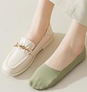 Een linker kuit en voet met een beige loafer met gouden gesp en een rechterkuit en voet met een mintgroene lage sok.