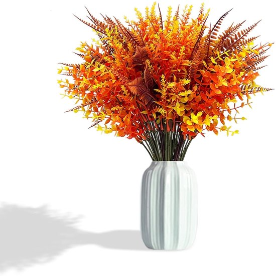 Un bouquet de plantes artificielles oranges, jaunes et brunes dans un vase blanc côtelé, avec de l'ombre en arrière-plan.