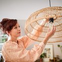 Vrouw met rood haar in een perzikkleurige top met stippen, kijkt naar een lamp.