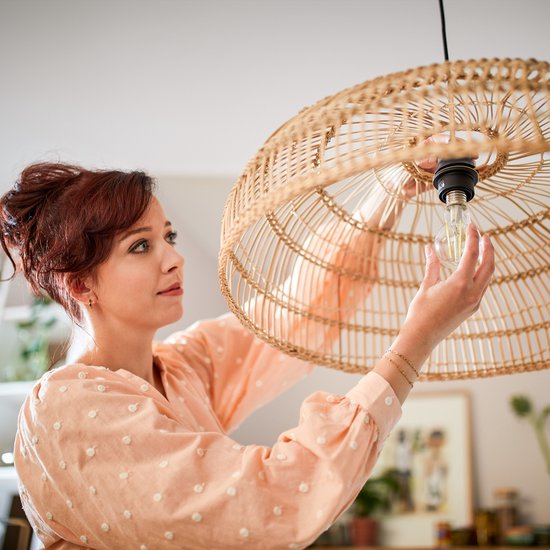 Vrouw met rood haar in een perzikkleurige top met stippen, kijkt naar een lamp.