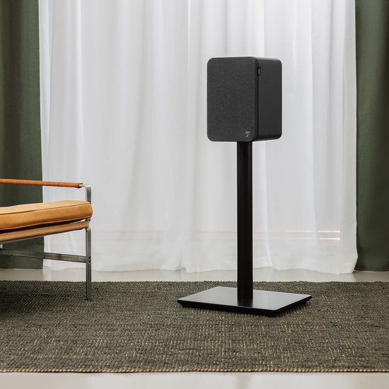Zwarte, compacte luidspreker op een zwarte standaard in een woonkamer.