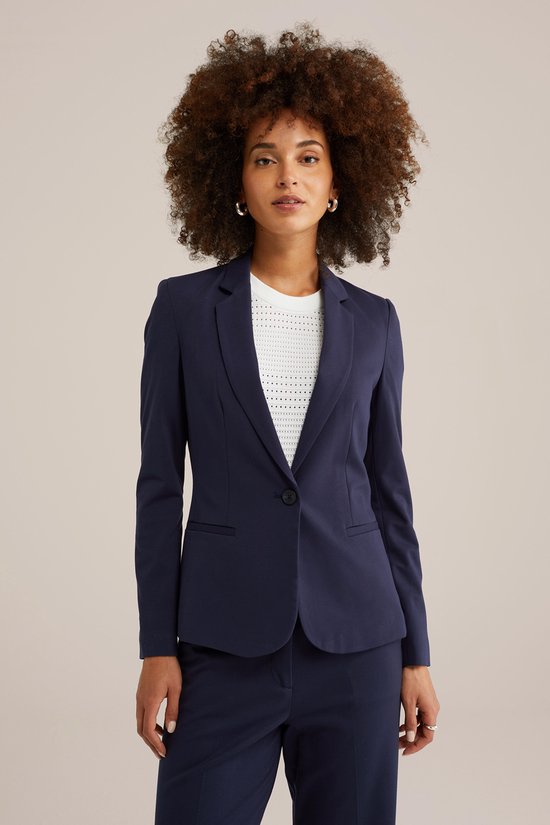 Model met donkerblauwe blazer, wit top met structuur en bijpassende broek.