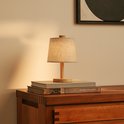Houten tafellamp met linnen kap, geplaatst op twee boeken op een houten kast.