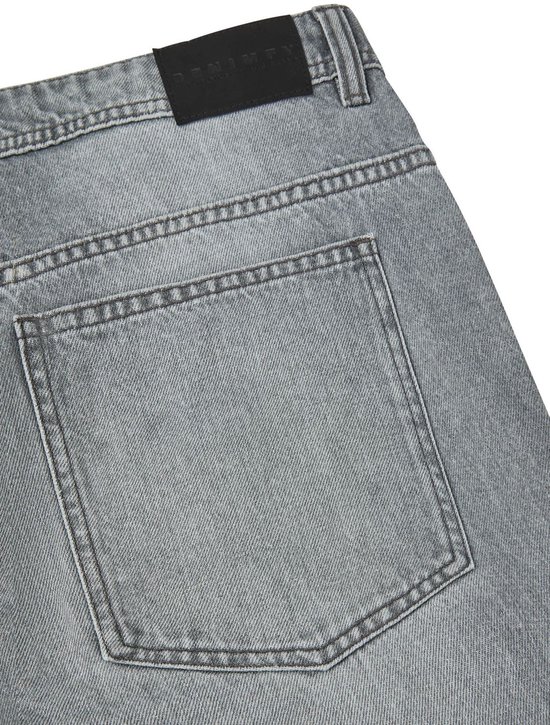 Detail van de achterkant van een losse grijze spijkerbroek met een zwart logo.