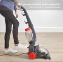 Grijze tapijtreiniger met rode wielen, staand model, een persoon sluit het snoer aan.