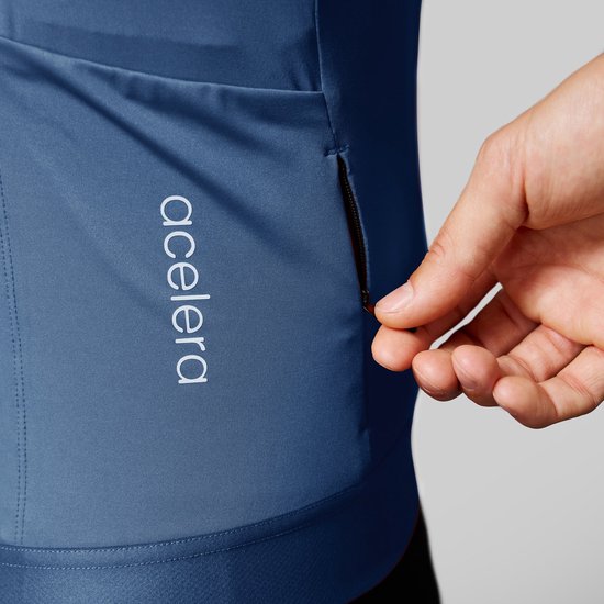 Detail van een blauw wielershirt met korte mouwen, met Acelera logo en een zak met rits.