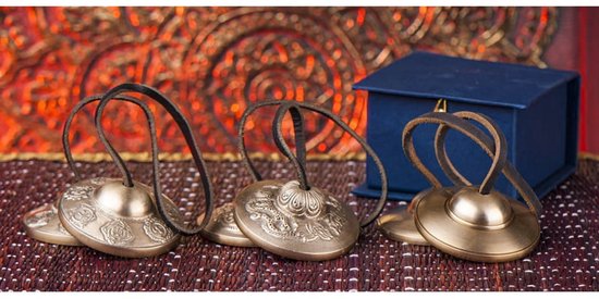 Trois cymbales tibétaines avec motif de dragon, à côté d'une boîte bleue.