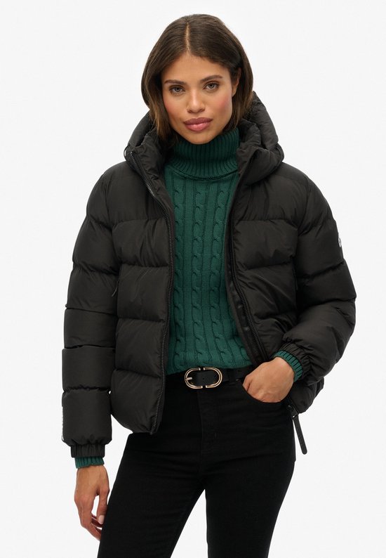 Model met zwarte Superdry pufferjas met capuchon, groene coltrui en riem.