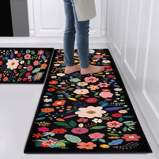 Personne pieds nus sur un tapis de cuisine noir avec un motif floral coloré.