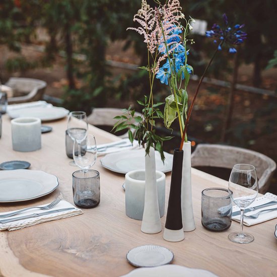 Gedekte tafel met drie keramieken vazen: wit, zwart en crèmekleurig, met bloemen.
