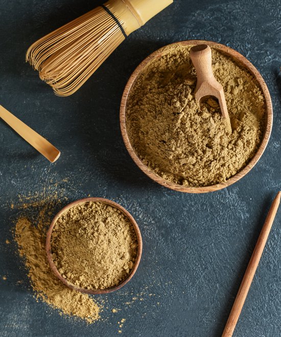 Houten kom gevuld met matcha poeder, met een houten schepje, een matcha klopper en een bamboe lepel ernaast.