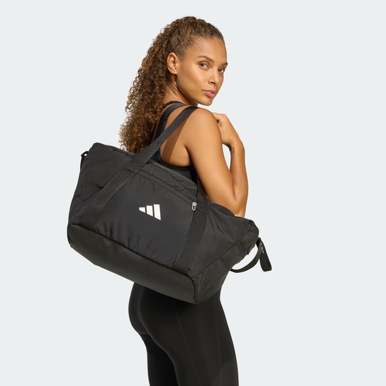 Vrouw met zwarte Adidas sporttas over de schouder gedragen.
