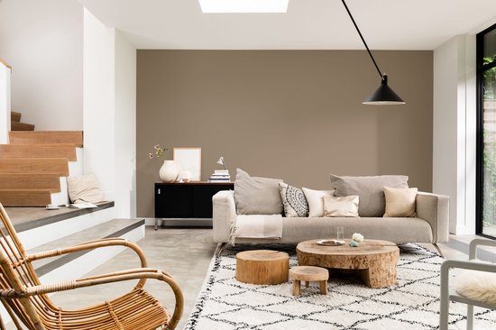 Woonkamer met beige bank, houten salontafel en een bruine muur.