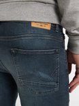 Man in grijze hoodie en donkerblauwe slim fit jeans, van achteren gezien.