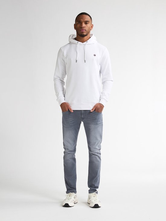Man van voren gezien, draagt een witte hoodie met ronde hals en grijze slim fit jeans.