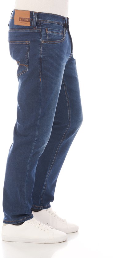 Donkerblauwe jeans van Mustang met oranje stiksels, gedragen door een model met witte sneakers.