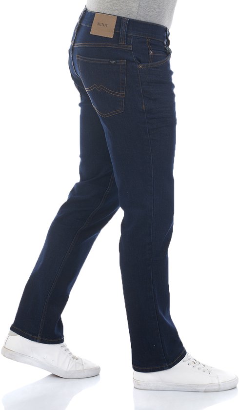 Donkerblauwe jeans met oranje stiksels en een bruine Mustang-patch op de achterkant. Model draagt witte sneakers.