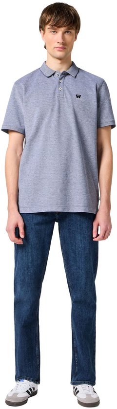 Man met een grijs polo shirt en een donkerblauwe jeans, witte sneakers.