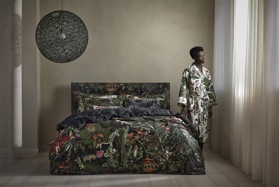 Model staat naast een bed, gekleed in een lichte badjas met jungleprint van bladeren en dieren.