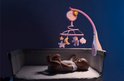 Baby ligt in een wieg met een roze muziekmobiel met maan, sterren en teddybeer.
