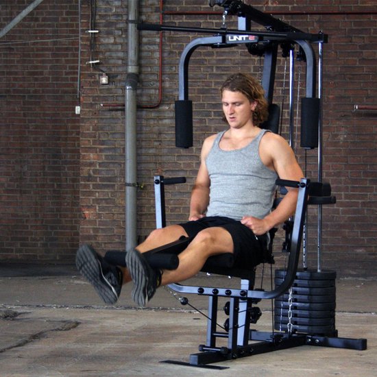 Man in grijze tanktop en zwarte short gebruikt de zittende been curl machine van een zwart krachtstation.
