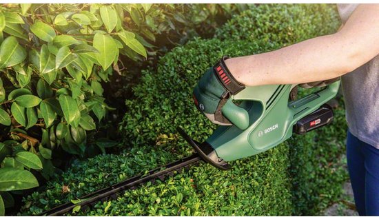 Vrouw met groene handschoenen snoeit struiken met een groene Bosch heggenschaar.