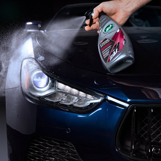 Main pulvérisant Turtle Wax Ceramic 3-en-1 Detailer sur le capot d'une voiture bleu foncé.