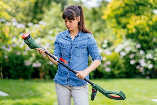Vrouw stelt Bosch grastrimmer in, met rode pijl die de instelling aangeeft.