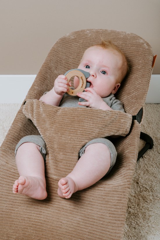 Baby met blauwe ogen en rood haar in een bruine corduroy wipstoel, bijt op een houten ring.
