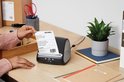 Dichte opname van een DYMO LabelWriter 5XL labelprinter op een bureau, met hand die label vasthoudt.
