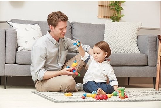 Een man en kind spelen op een kleed met magnetisch constructiespeelgoed, waaronder een vishengel.