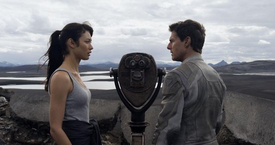 Tom Cruise en Olga Kurylenko kijken elkaar aan bij een telescoop.