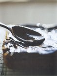 Lepel met chocoladeglazuur op een stuk gebak, op een rooster.