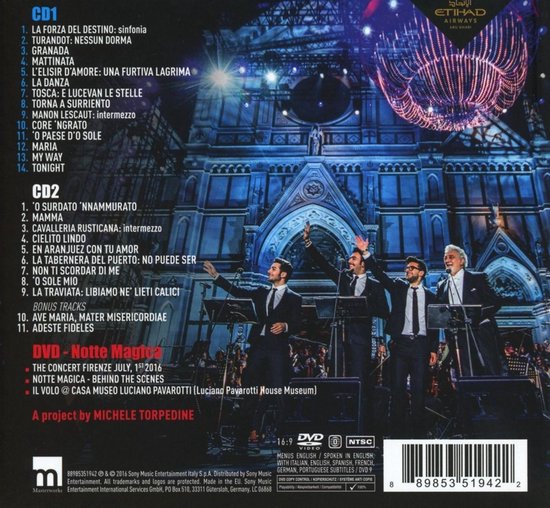 Vier mannen in smoking, waaronder Placido Domingo, zingen met opgeheven armen op een podium met orkest en verlichting. Achtergrond toont Florence.