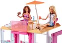 Twee Barbie poppen op een zonneterras met paraplu en drankjes.