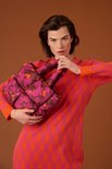 Model met bruine puffy handtas met paarse en oranje bloemenprint, gedragen met een oranje/roze jurk.