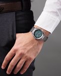 Man met een zilverkleurig Citizen horloge met blauwgroene wijzerplaat om de pols.