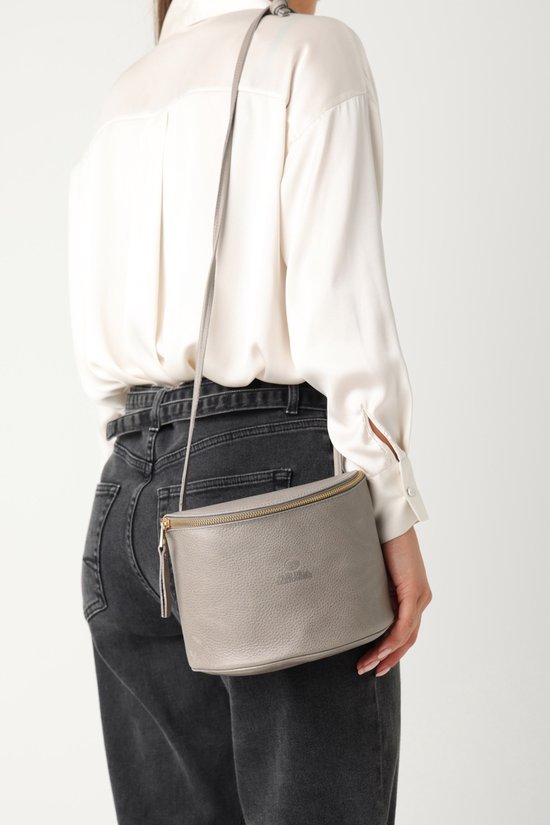 Vrouw met grijze leren crossbody tas, gedragen over de schouder.