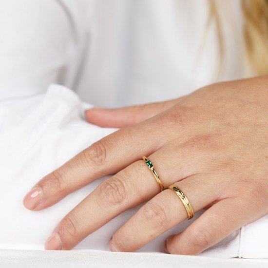 Hand van een vrouw met twee gouden ringen: een met smaragdgroene steen, de ander met bladerpatroon.