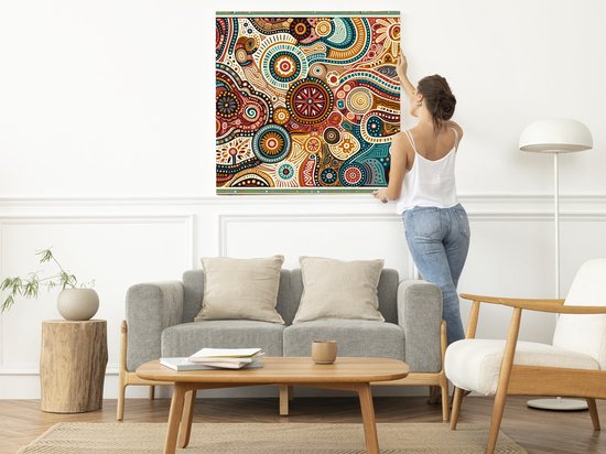 Vrouw hangt een abstract schilderij op met complexe patronen in rood, bruin, blauw en beige.