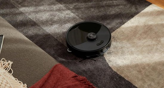 Zwarte ronde robotstofzuiger op een grafisch vloerkleed met bruine en beige vlakken.