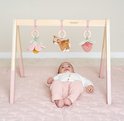 Baby ligt onder houten babygym met speeltjes: bloem, hertje en aardbei.