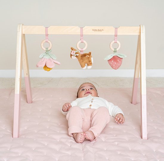 Baby ligt onder houten babygym met speeltjes: bloem, hertje en aardbei.