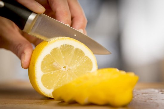 Een hand snijdt een citroen in tweeën met een Tefal koksmes.