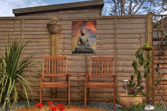 Bouddha en pierre sur fleur de lotus sur fond de coucher de soleil orange, suspendu à une clôture en bois avec deux chaises en bois.