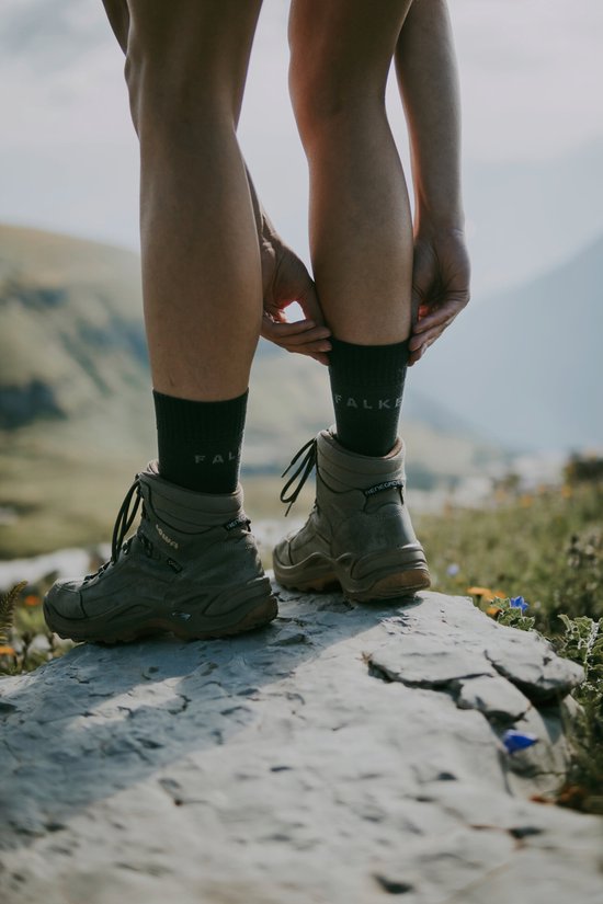 Twee vrouwenbenen in donkergrijze Falke sokken en leren wandelschoenen, staand op een rots.